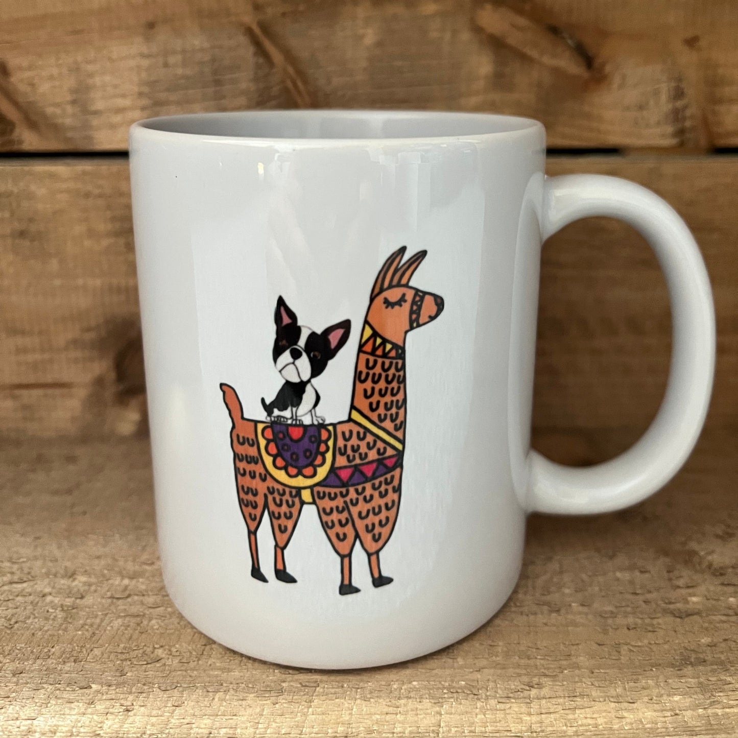 White mug with decorative design of a dog and two llamas on a wooden surface