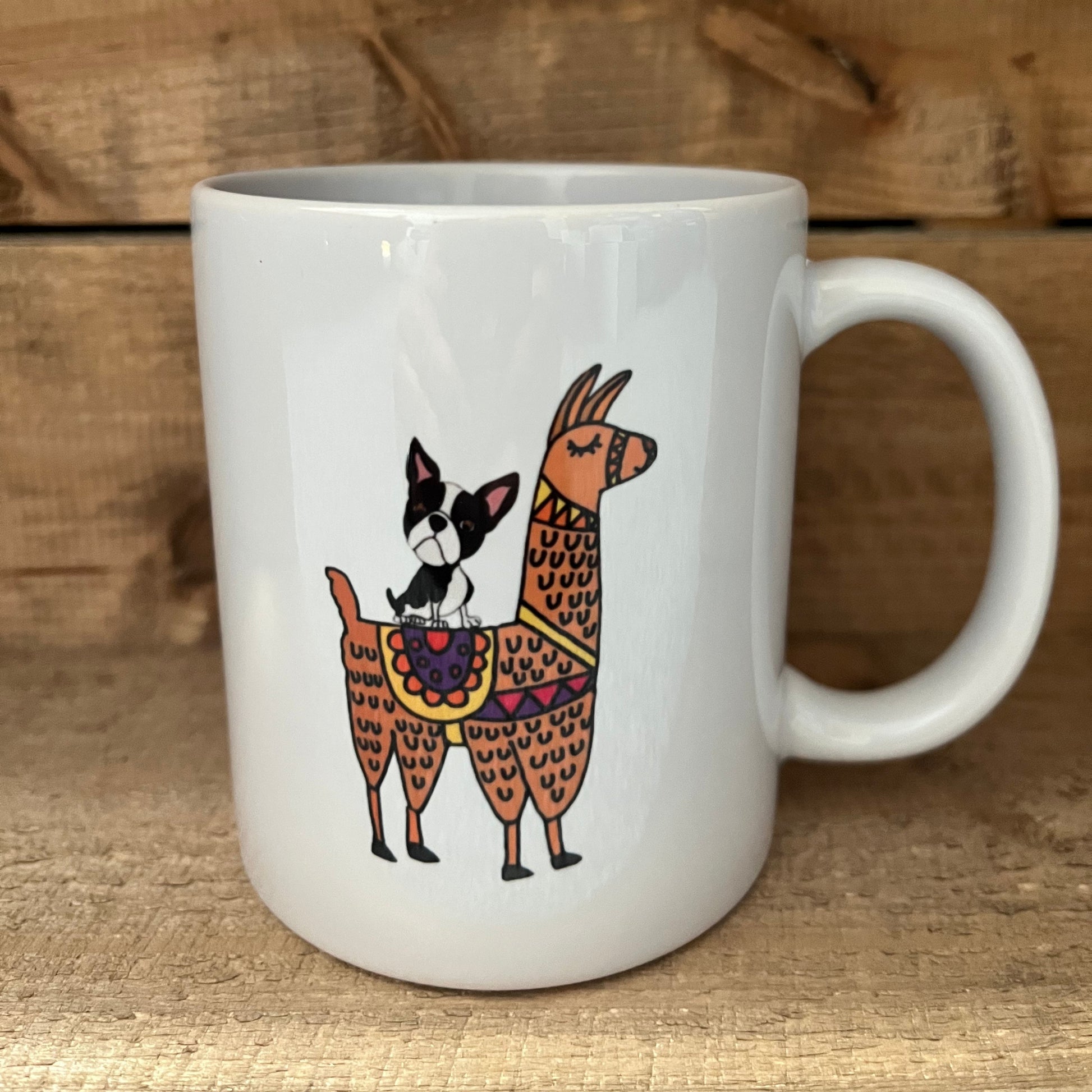 White mug with decorative design of a dog and two llamas on a wooden surface